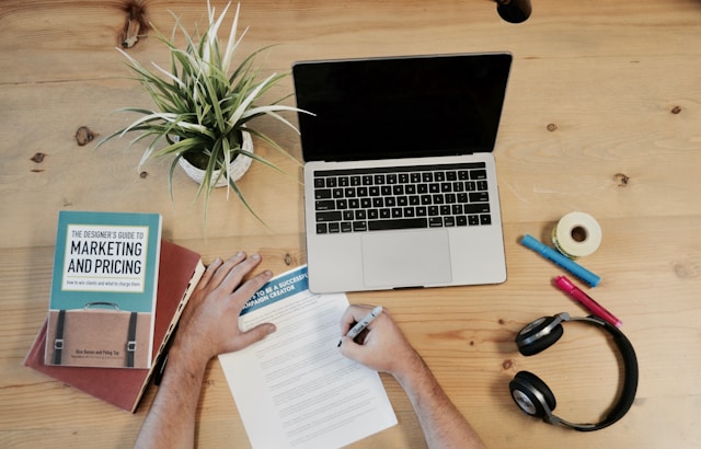 A person working in front of a computer next to a book titled “Marketing and Pricing.”