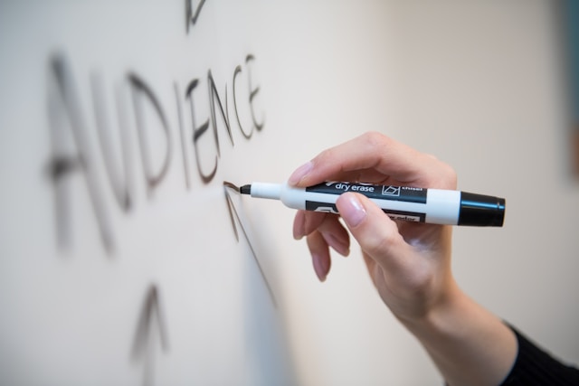 A person writing the word audience on a whiteboard. 