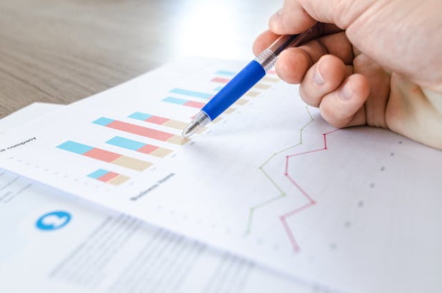 A person pressing a pen against paper that’s showing data. 