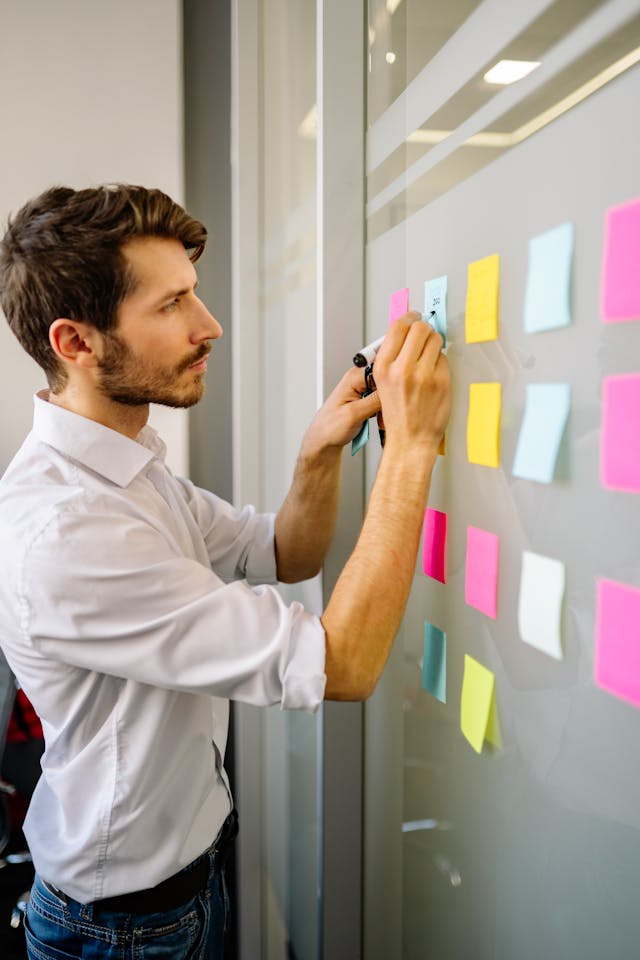 A person writing on sticky notes against a wall. 