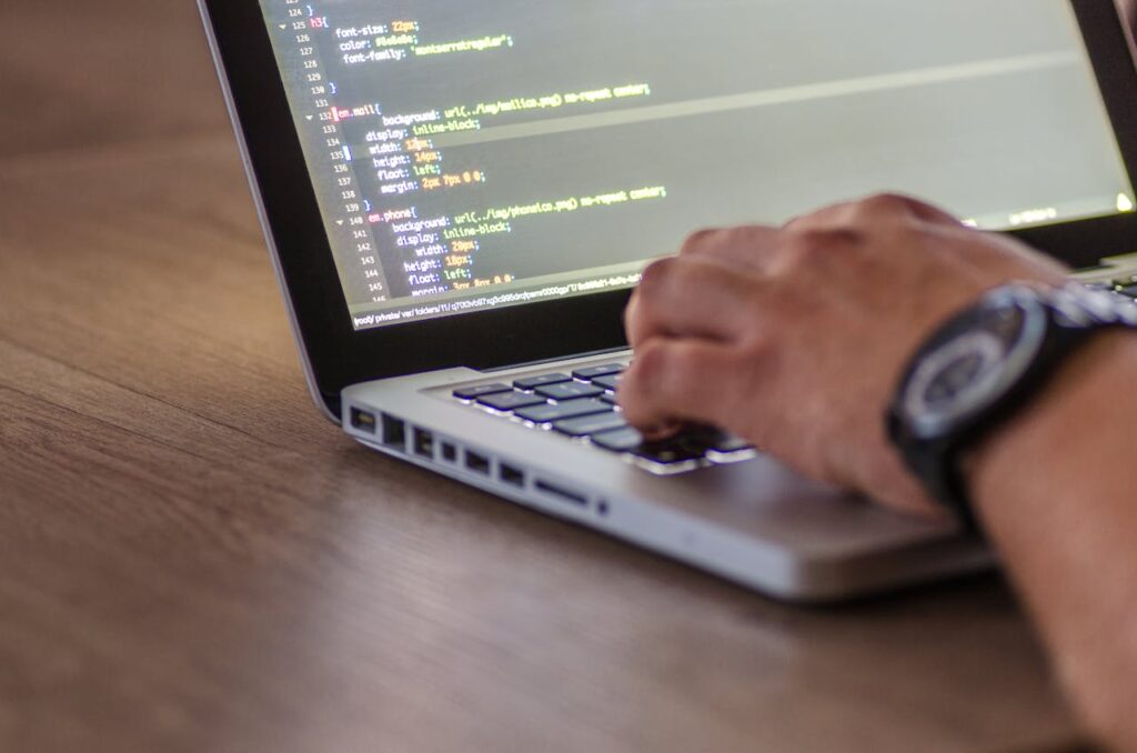 A person typing on a laptop with code showing on the screen.